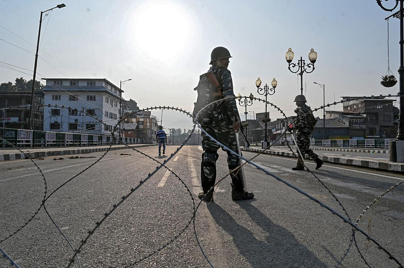 Paramilitary troopers stand guard behind a barbed fence wire as they block a road during a curfew in Srinagar. (AFP Photo)