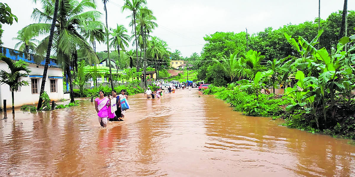 People cross a flooded road in Belthangady.