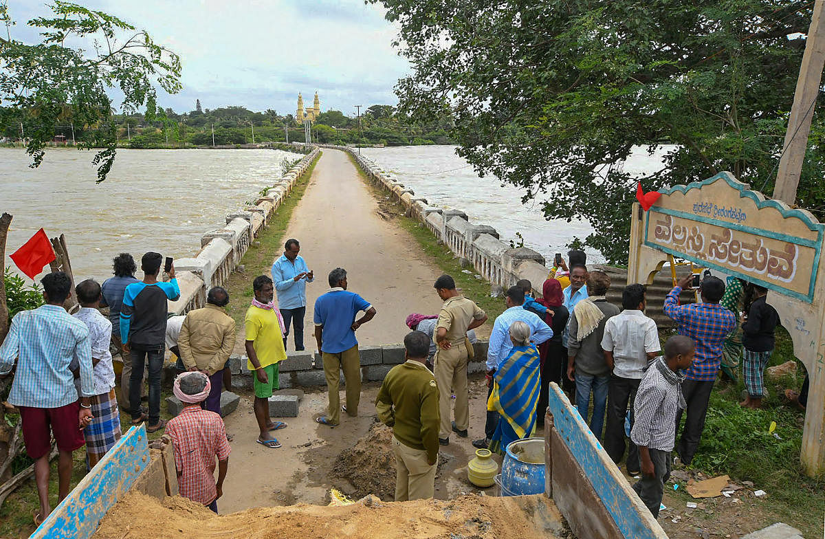 Visitors stand near the Wellesley Bridge over flooded Cauvery river, in Mandya, Sunday, Aug 11, 2019. PTI