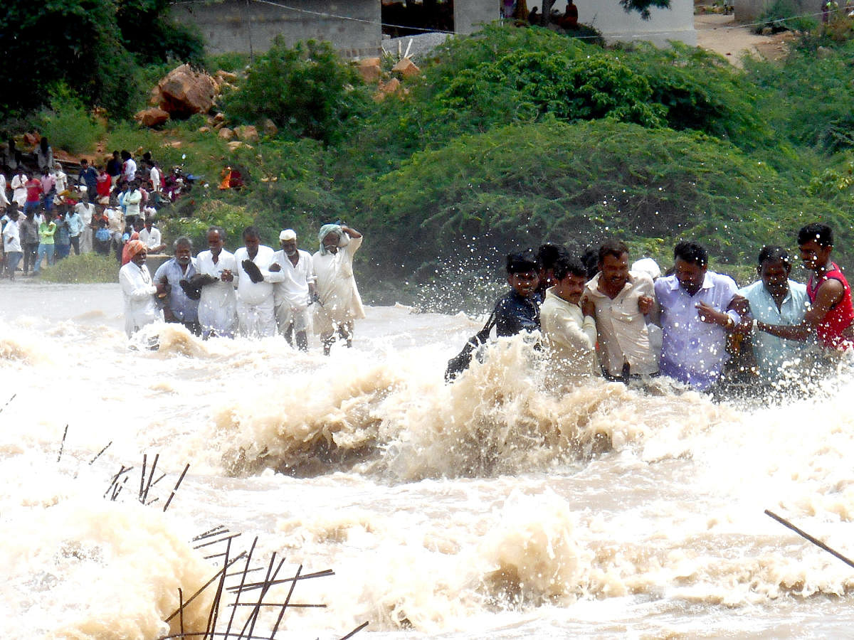 Villagers stranded at Jaladurg village in Lingasugur taluk of Raichur district cross the swollen Krishna river on inundated bridge on Thursday. DH PHOTO/B A NANDIKOLMATH