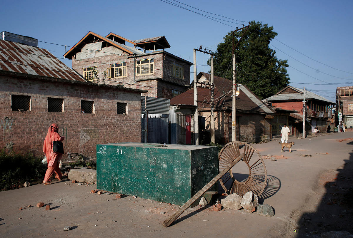 A Kashmiri woman walks past a blockade put up by residents to prevent security forces from entering their neighborhood during restrictions, in Srinagar. (Reuters Photo)