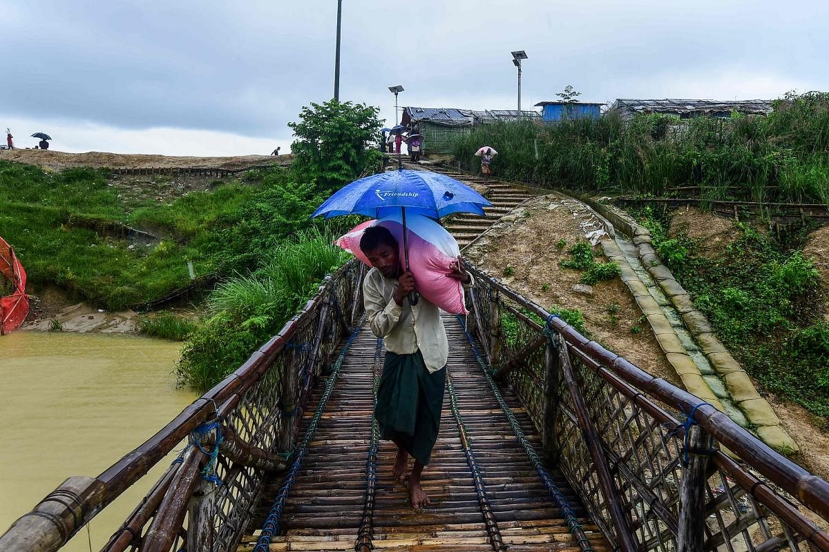 A Rohingya man shelters from the rain as he carries relief aid at the Kutupalong Rohingya refugee camp in Bangladesh's Ukhia district on August 24, 2019. (Photo by AFP)