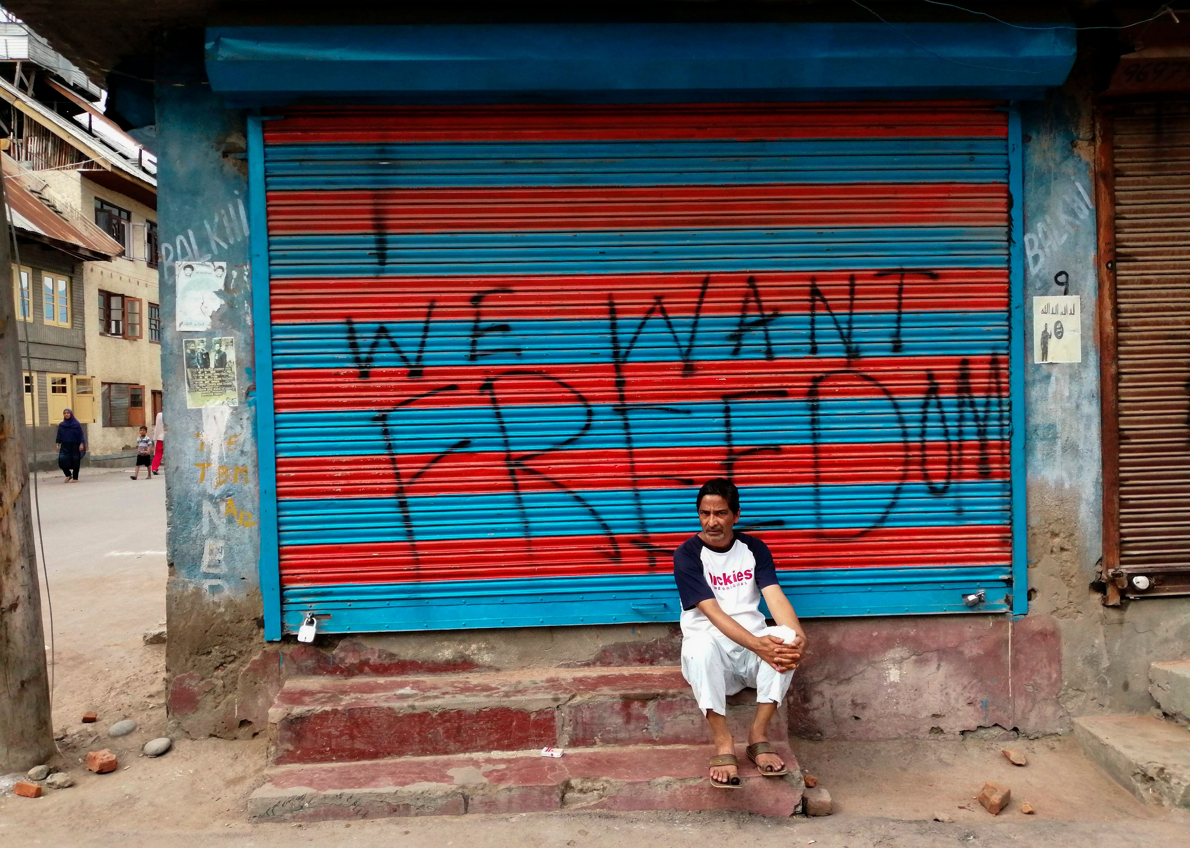  a man sits next to graffiti that reads "We Want Freedom" on a shuttered store in the Soura locality in Srinagar, during the lockdown. Photo by Jalees ANDRABI / AFP
