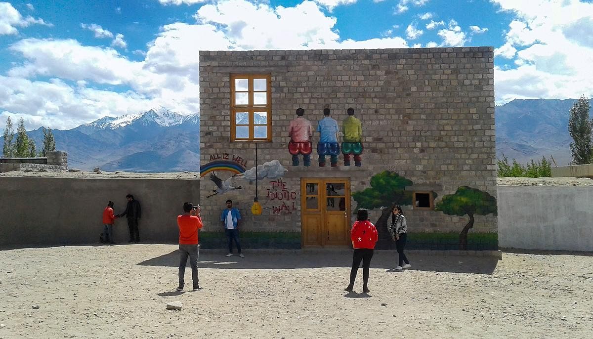 Tourists pose for pictures at a duplicate 'Rancho's Wall' on the premises of Druk Padma Karpo School at Shey in Leh district of Ladakh. (PTI Photo)