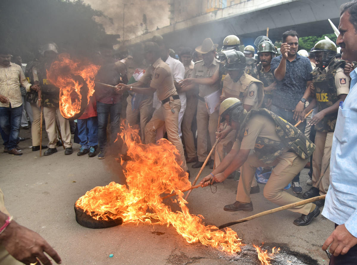 Policemen attempt to douse a burning tyre set on fire by Congress workers condemning the arrest of party leader D K Shivakumar, in Bengaluru on Wednesday. DH Photo