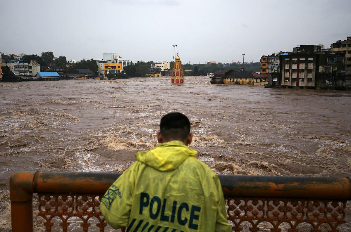 A policeman stands on a bridge as temples and houses are seen submerged in the waters of overflowing river Godavari after heavy rainfall in Nashik (Reuters Photo)