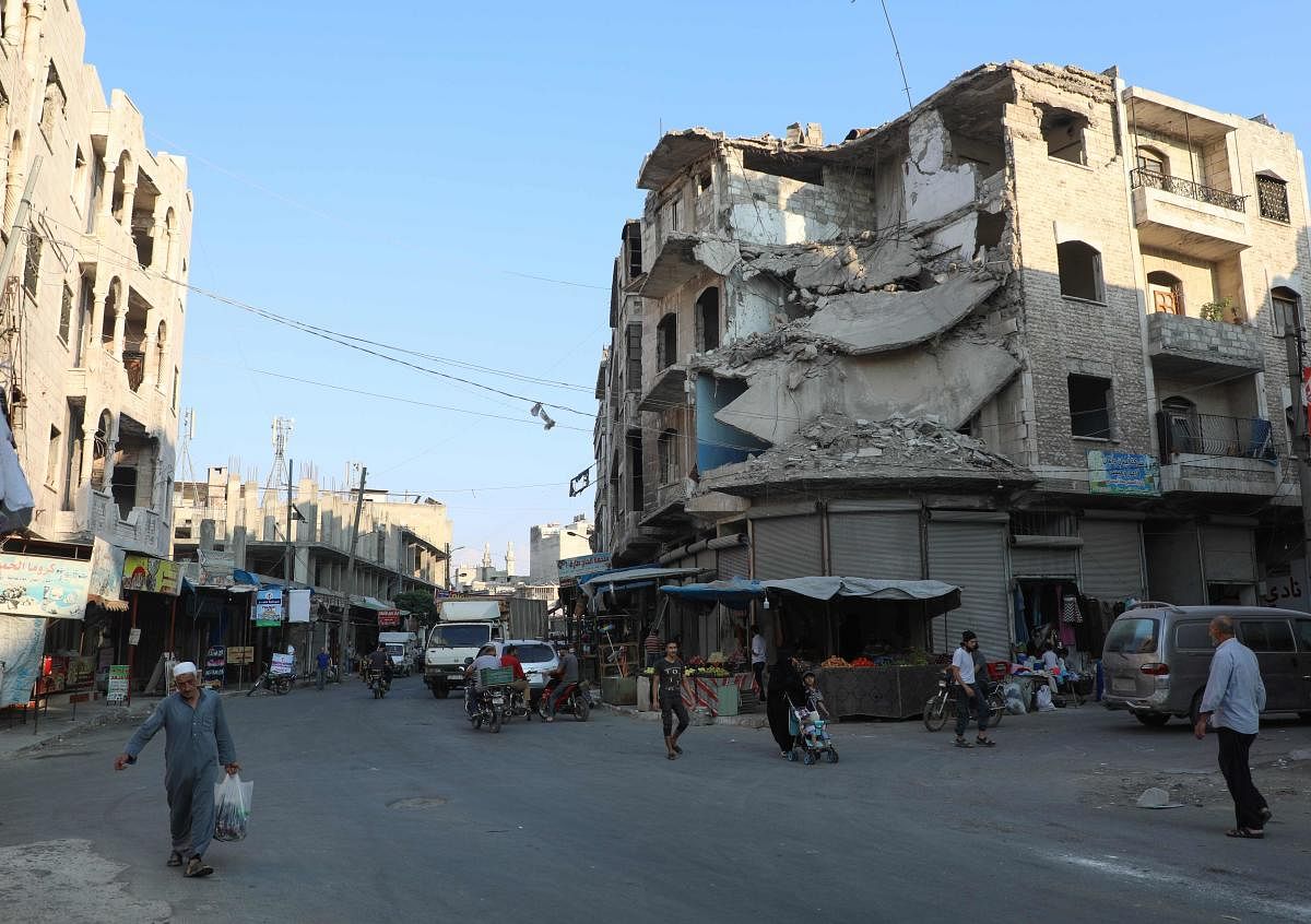 People walk near heavily damaged buildings in the rebel-held city of Idlib (AFP Photo)