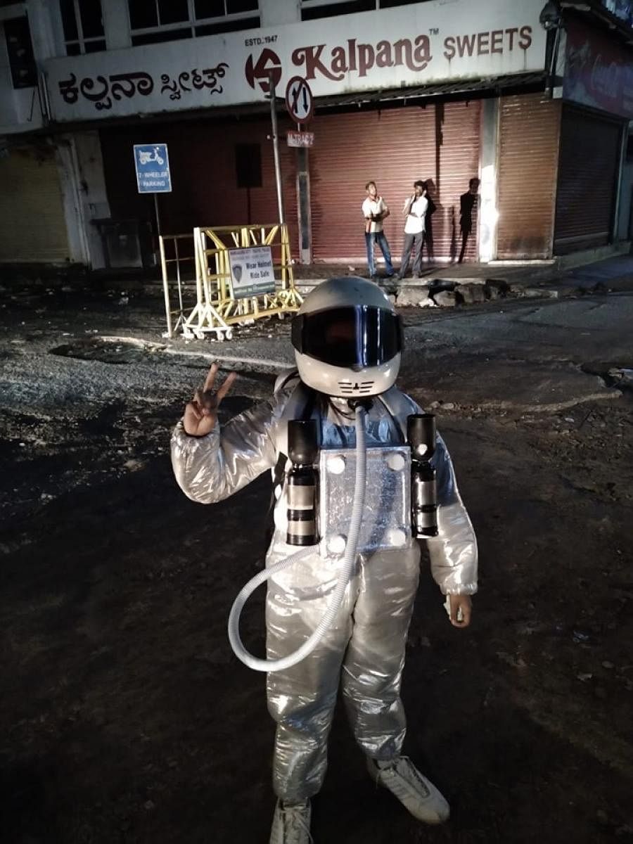 Adlin D’Silva, dressed like an astronaut, walks on a pothole-ridden road at Central Market in Mangaluru.