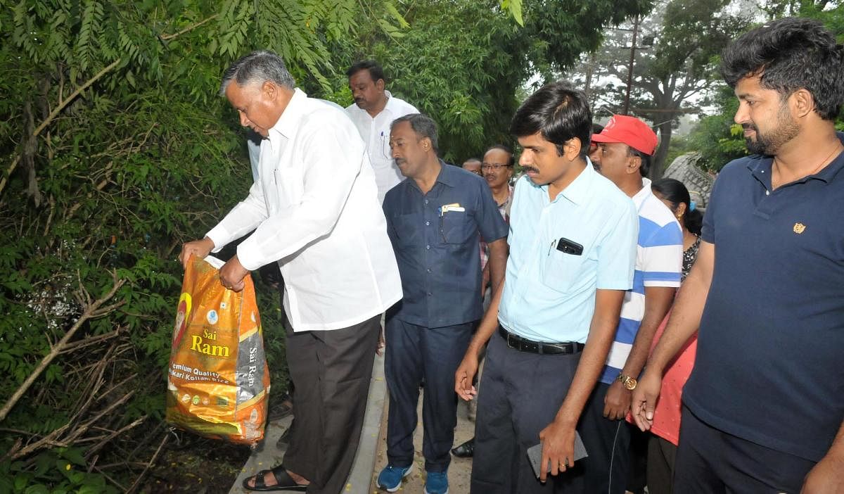 District In-charge Minister V Somanna lifts a bag containing waste atop the Chamundi Hill in Mysuru on Saturday. Deputy Commisisoner Abhiram G Sankar and MP Pratap Simha are seen. dh photo