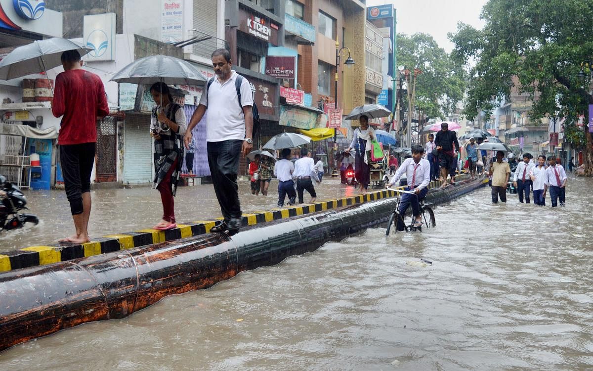 Varanasi: Pedestrians walk through a waterlogged road following heavy rainfall, in Varanasi. (PTI Photo)