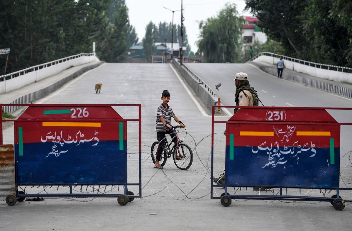 An Indian soldier (R) stands guard next to a barricade on a deserted street as a child on a bicycle looks on during a curfew in Srinagar. (AFP Photo)