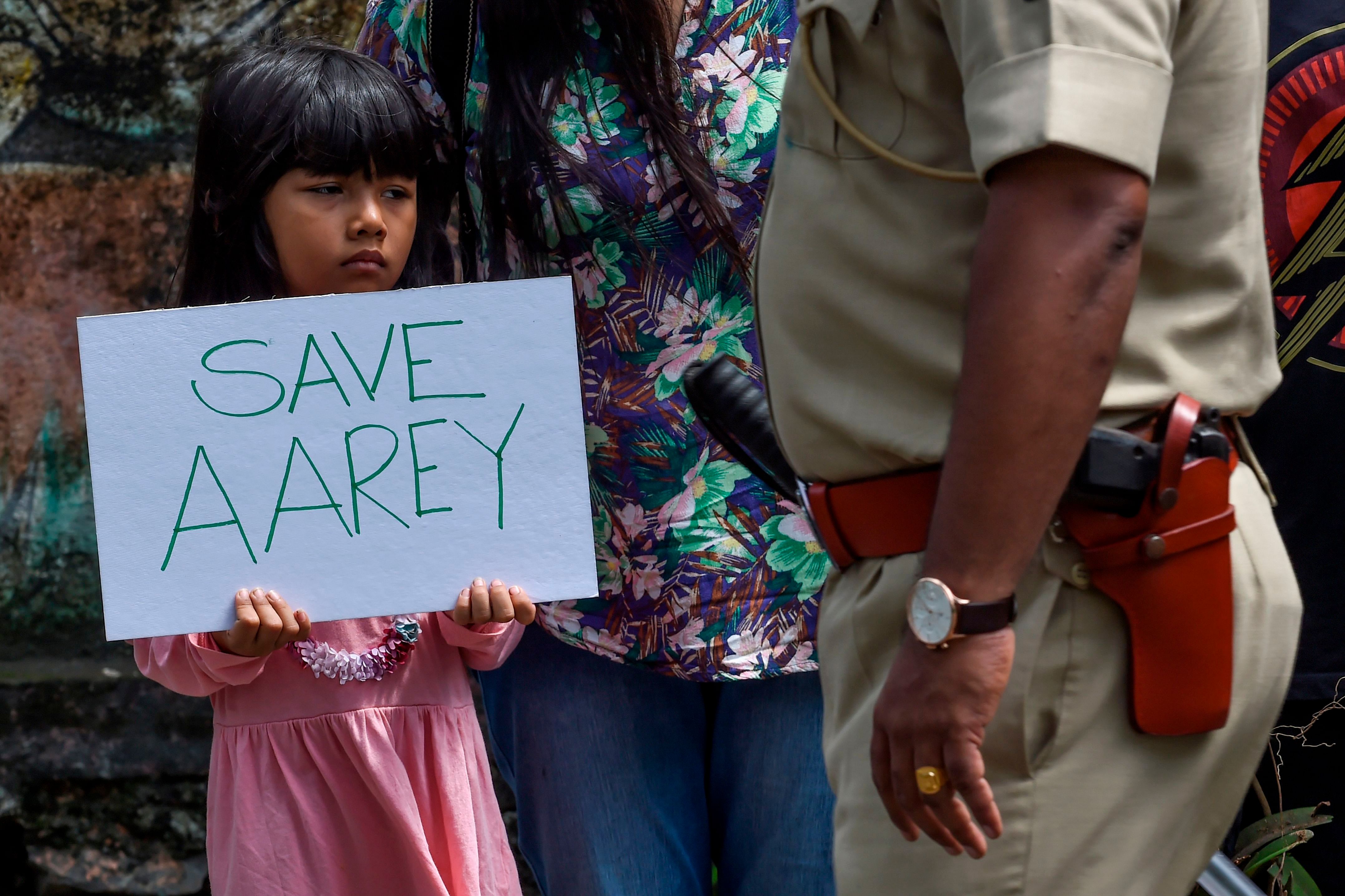 A policeman walks past a child holding a poster as she protests against the destruction of Aarey forest which they call "Mumbai's Amazon", after the government approved cutting down 2,700 trees for constructing a metro train car shed, in Mumbai. (AFP Photo)