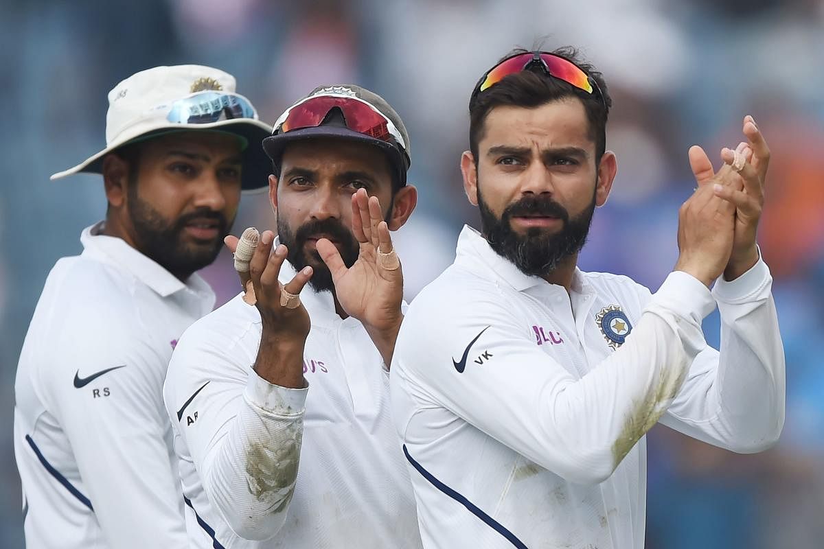 Indian team captain Virat Kohli (R), Ajinkya Rahane (C) and Rohit Sharma gesture towards fans as they celebrate on the fourth day of play after winning the second Test cricket match against South Africa, at the Maharashtra Cricket Association Stadium in Pune on October 13, 2019. (Photo by PUNIT PARANJPE / AFP)