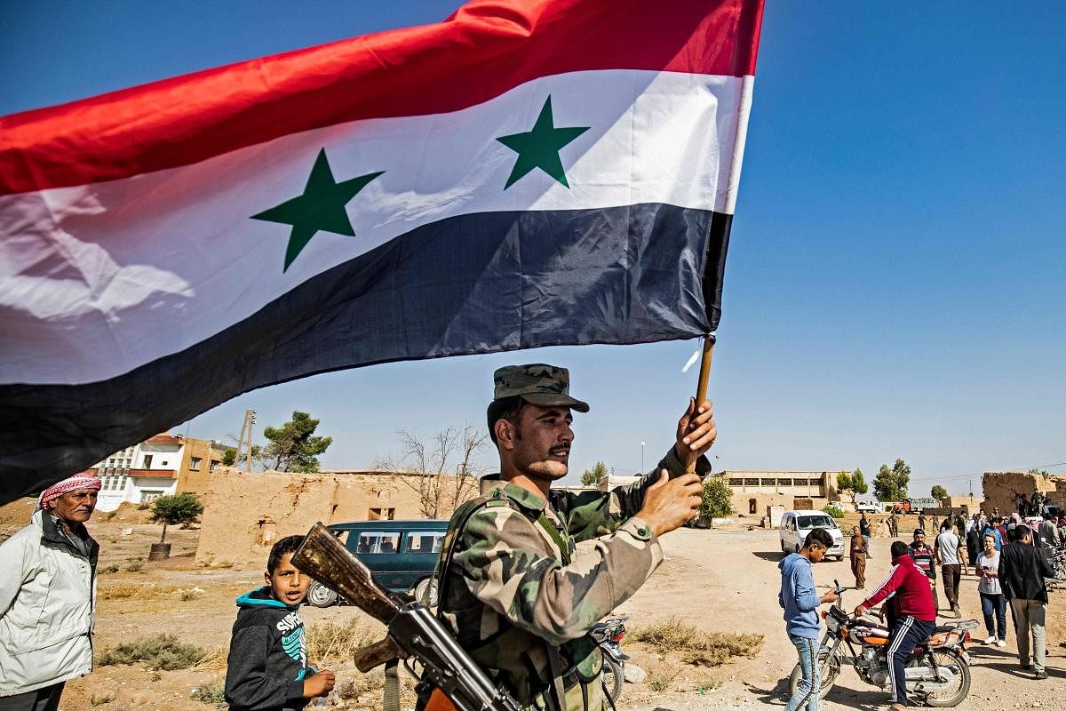 A Syrian regime soldier waves the national flag a street on the western entrance of the town of Tal Tamr in the countryside of Syria's northeastern Hasakeh province on October 14, 2019.(AFP)