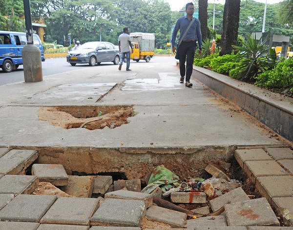 Pedestrians walk near a bad footpath on the TenderSure Vittal Mallya Road in Bengaluru on Tuesday. (DH Photo: Pushkar V)