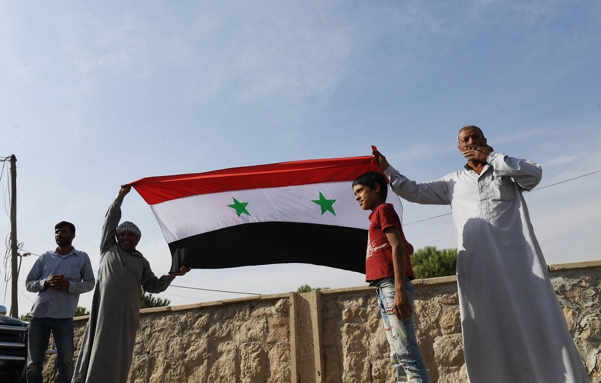 Locals hold the Syrian national flag in the village of al-Sultaniyah on the outskirts of the town of Manbij, which is now controlled by Syrian regime forces. (Photo by AFP)