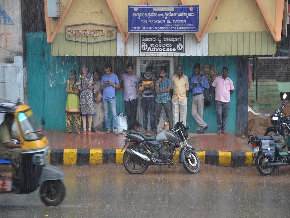 People take shelter under at a building on PB Road in Gadag on Thursday. Gadag town  received light showers intermittently. DH PHOTO
