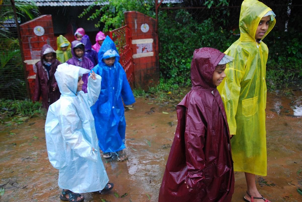 Schoolchildren are on their way back home, with raincoats on, in Madikeri on Tuesday evening.
