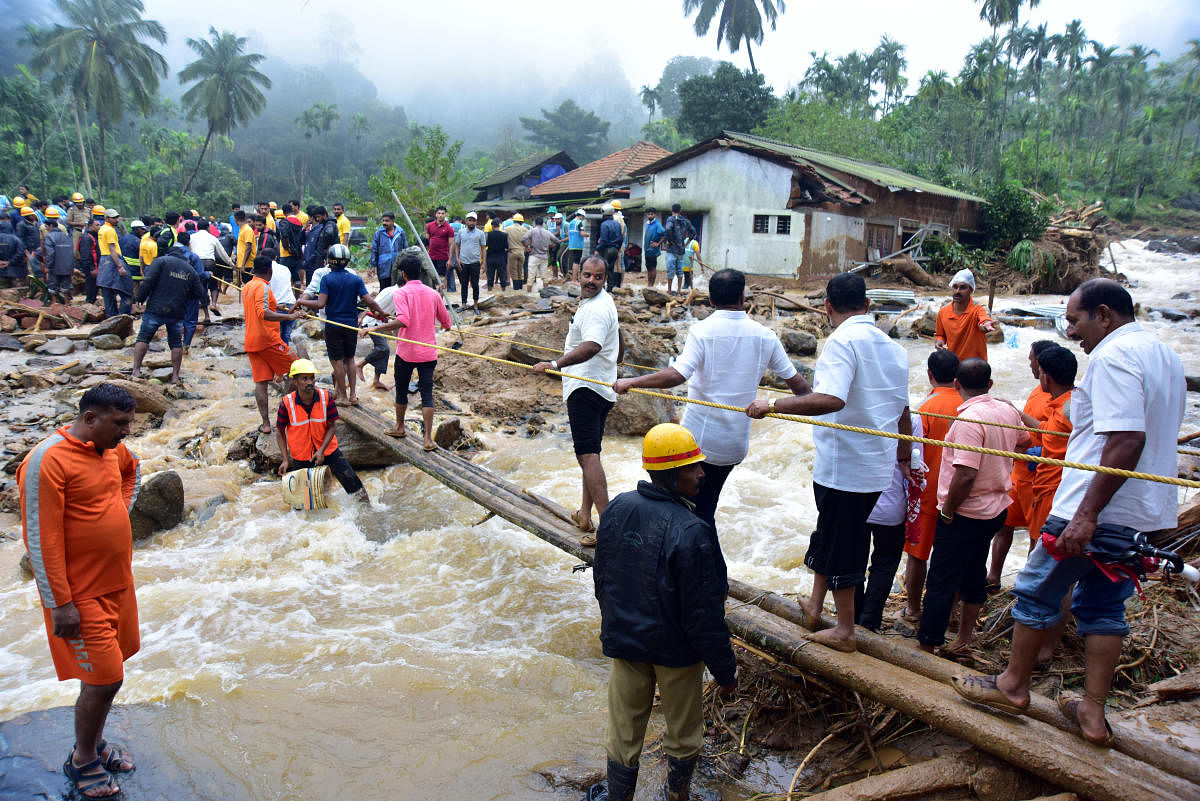People cross a makeshift bridge across a stream that sprung up after rain and a landslide at Jodupala in Kodagu district. DH PHOTO