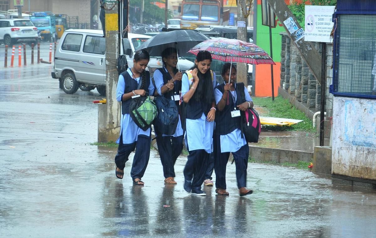 Students walk amid the rain at Hanumantappa Circle in Chikkamagaluru city on Tuesday.