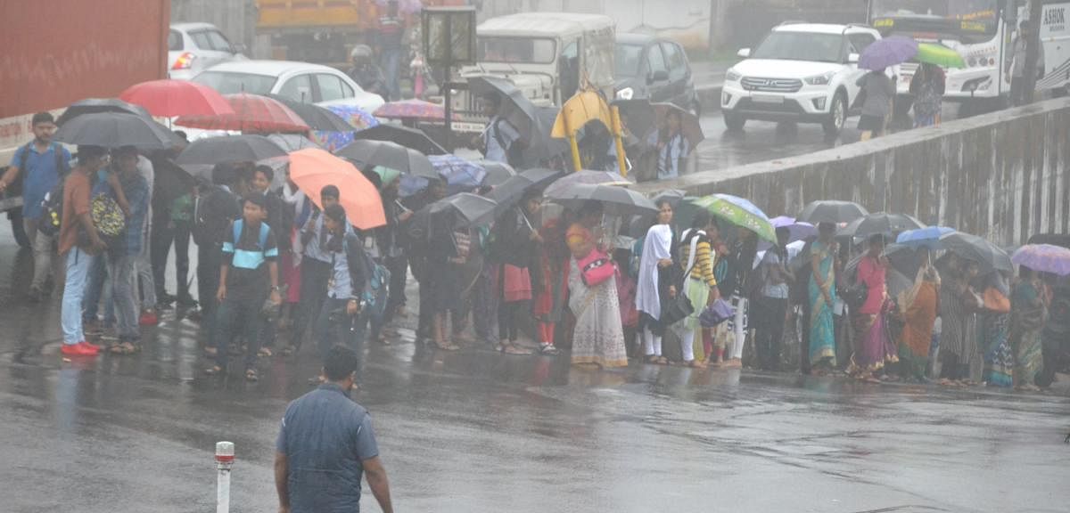 People were seen waiting for buses during heavy rain at General Thimayya Circle in Madikeri on Wednesday.