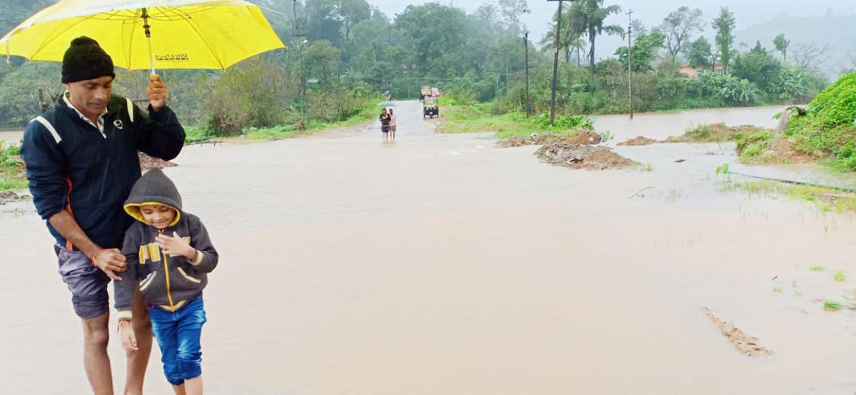 A man and a child walk on the submerged Bhagamandala-Ayyangeri Road.