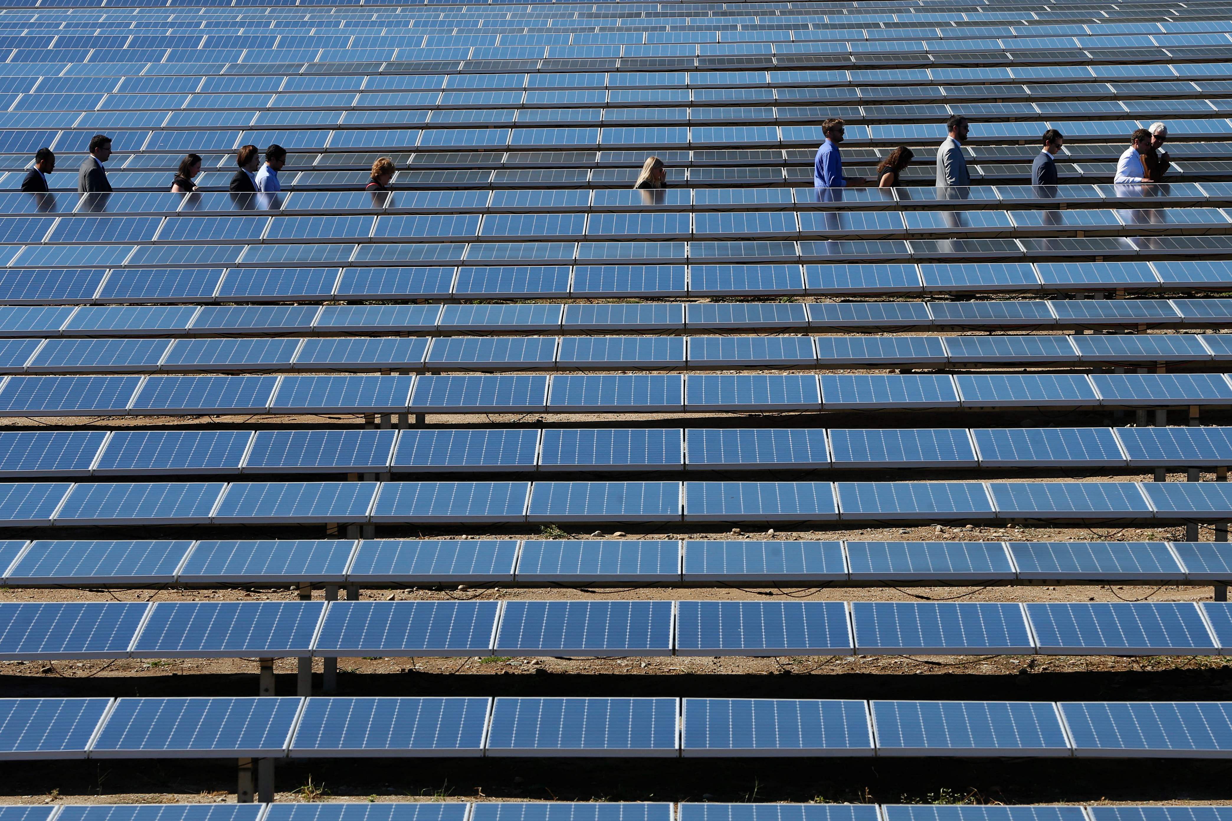 People walk between solar panels during the inauguration of a solar farm in Giuncaggio. (AF Photo)