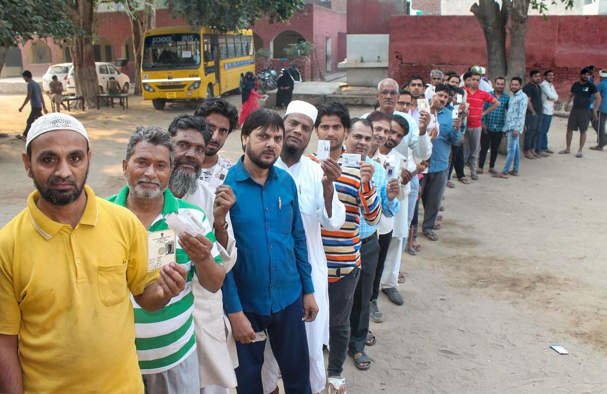 Voters stand in a queue and show their voting cards as they wait to cast their votes at a polling station for the Haryana Assembly elections, at Badkal in Faridabad, Monday, Oct. 21, 2019. (PTI Photo)