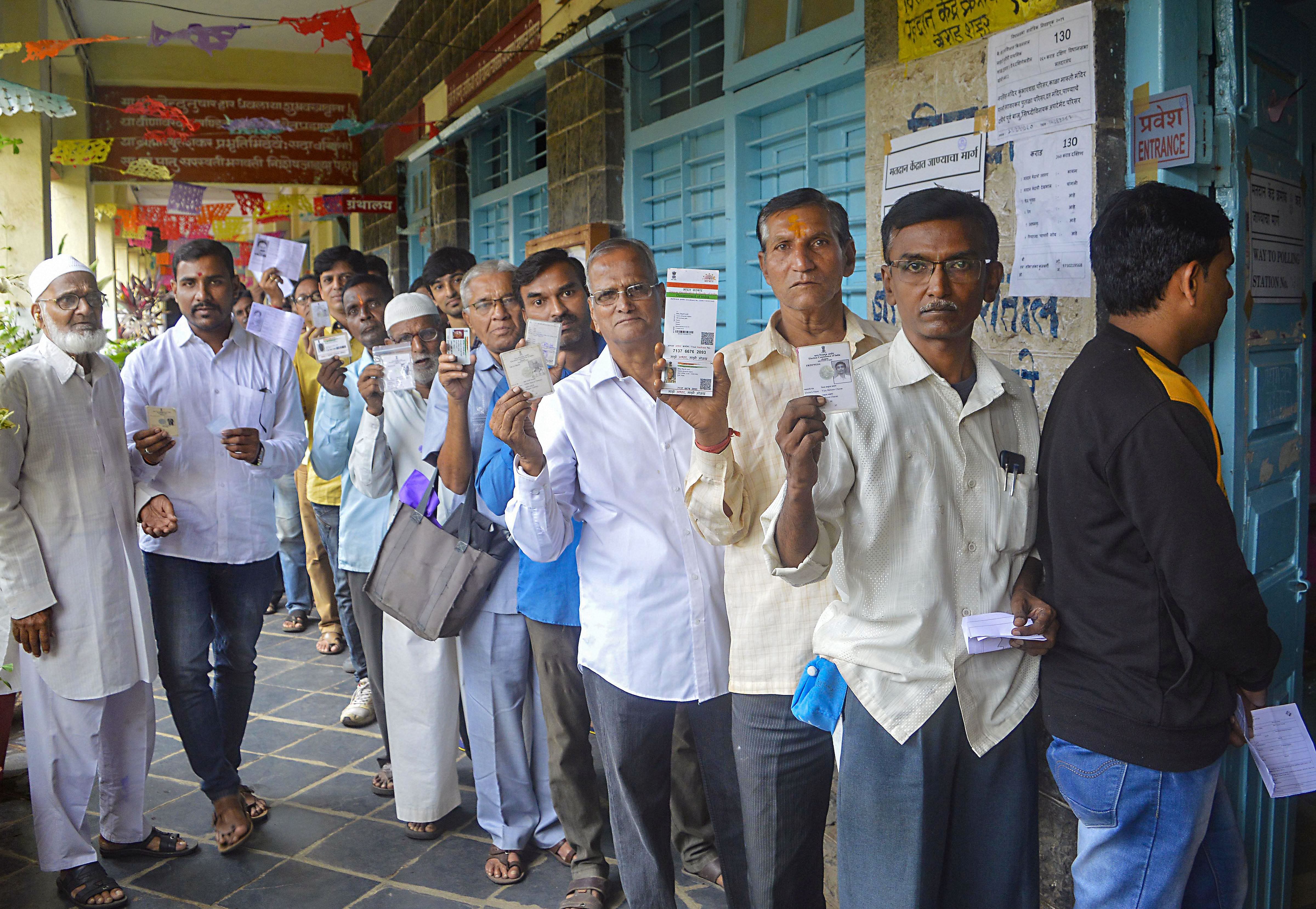Voters stand in a queue and show their voting cards as they wait to cast their votes at a polling station for the Maharashtra Assembly elections. (PTI Photo)