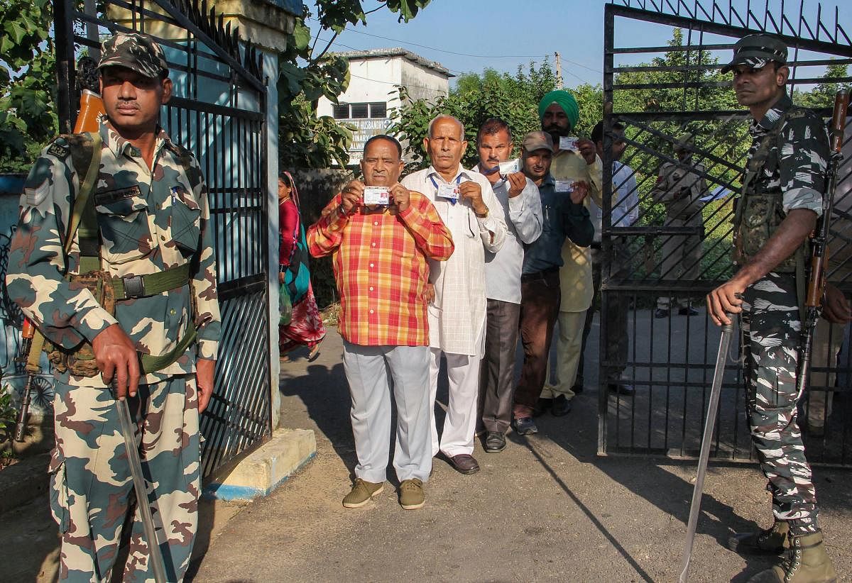Security personnel stand guard as panchs and sarpanchs queue up to cast their votes for Block Development Committees (BDC) elections in Kashmir (PTI Photo)