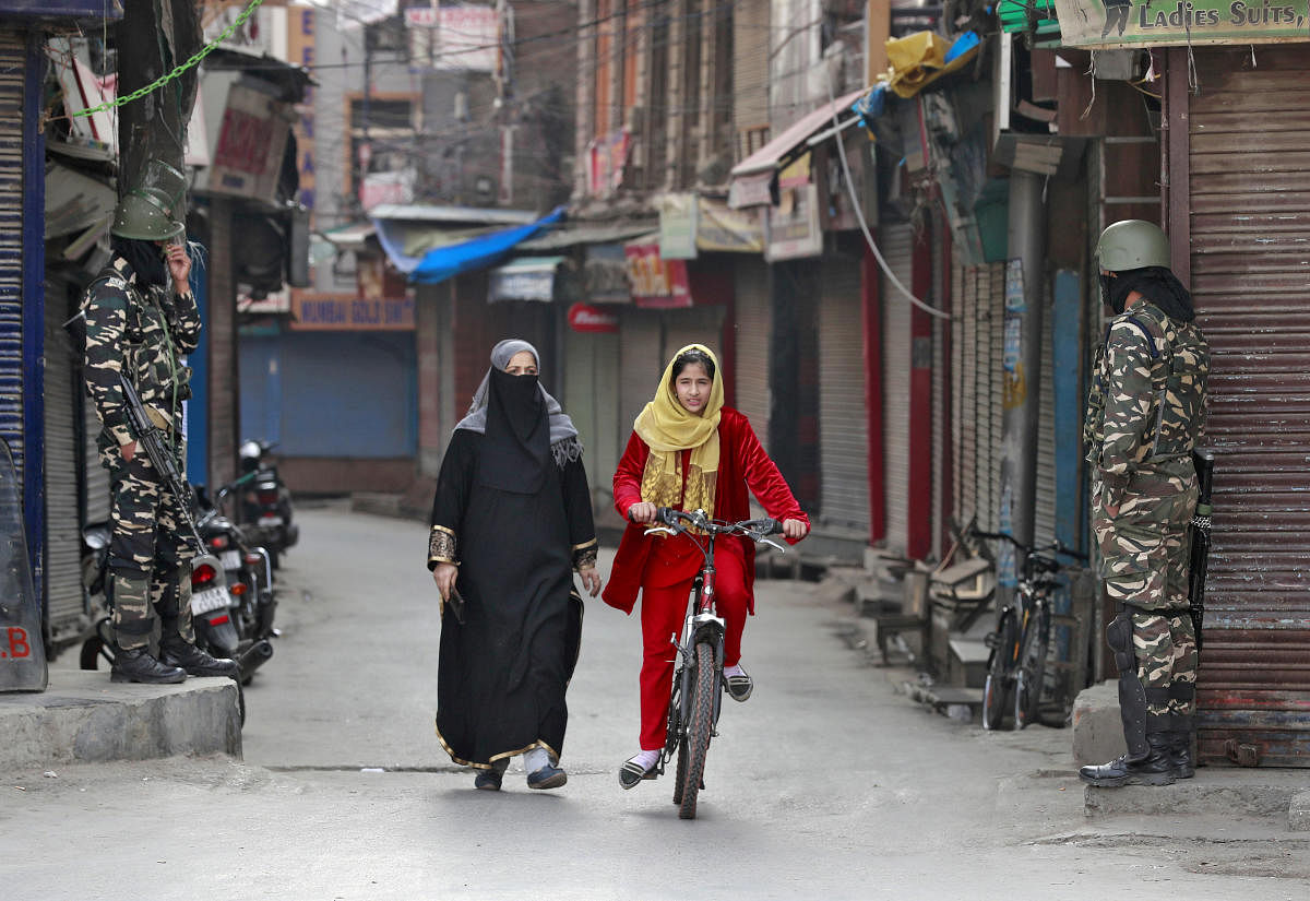 A Kashmiri girl rides her cycle past security force personnel standing guard in front of closed shops in a street in Srinagar on October 30, 2019. Reuters