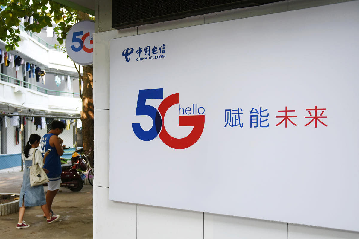 People holding their mobile phones walk past a China Telecom 5G sign at a university in Haikou, Hainan province, China. Reuters file photo