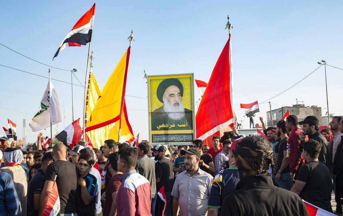 Iraqi demonstrators carry flags and an image of Shiite cleric Ayatollah Ali Husaini al-Sistani, during ongoing anti-government protests. (Photo AFP)