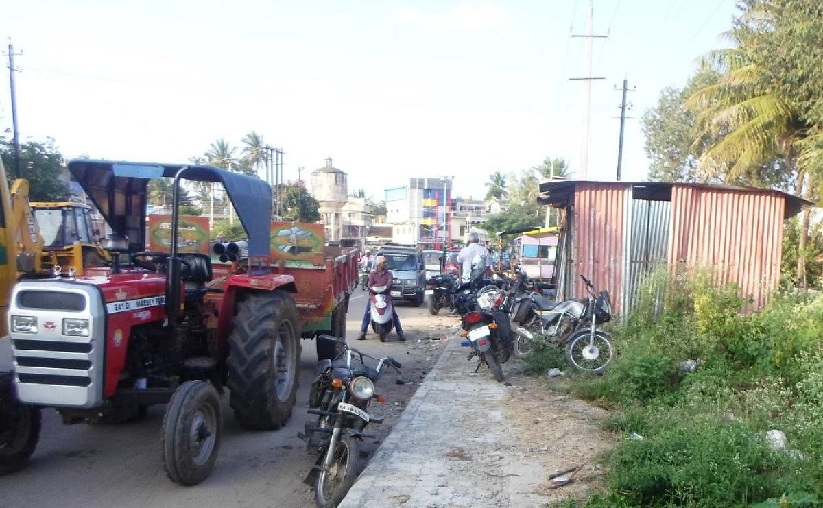 Petty shops and parked vehicles on the footpath on Ajjampura-Birur Road.