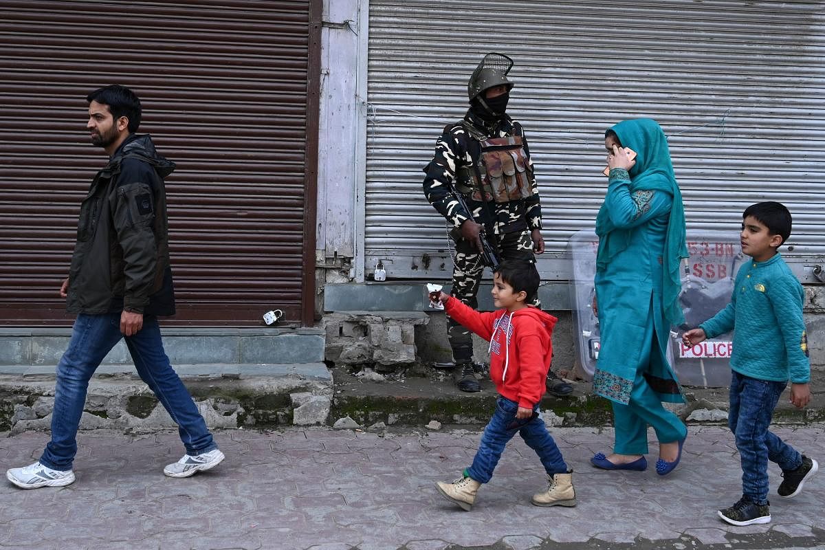 An Indian security personnel stands guard as pedestrians walk past during a lockdown in Srinagar on November 5, 2019. (AFP)