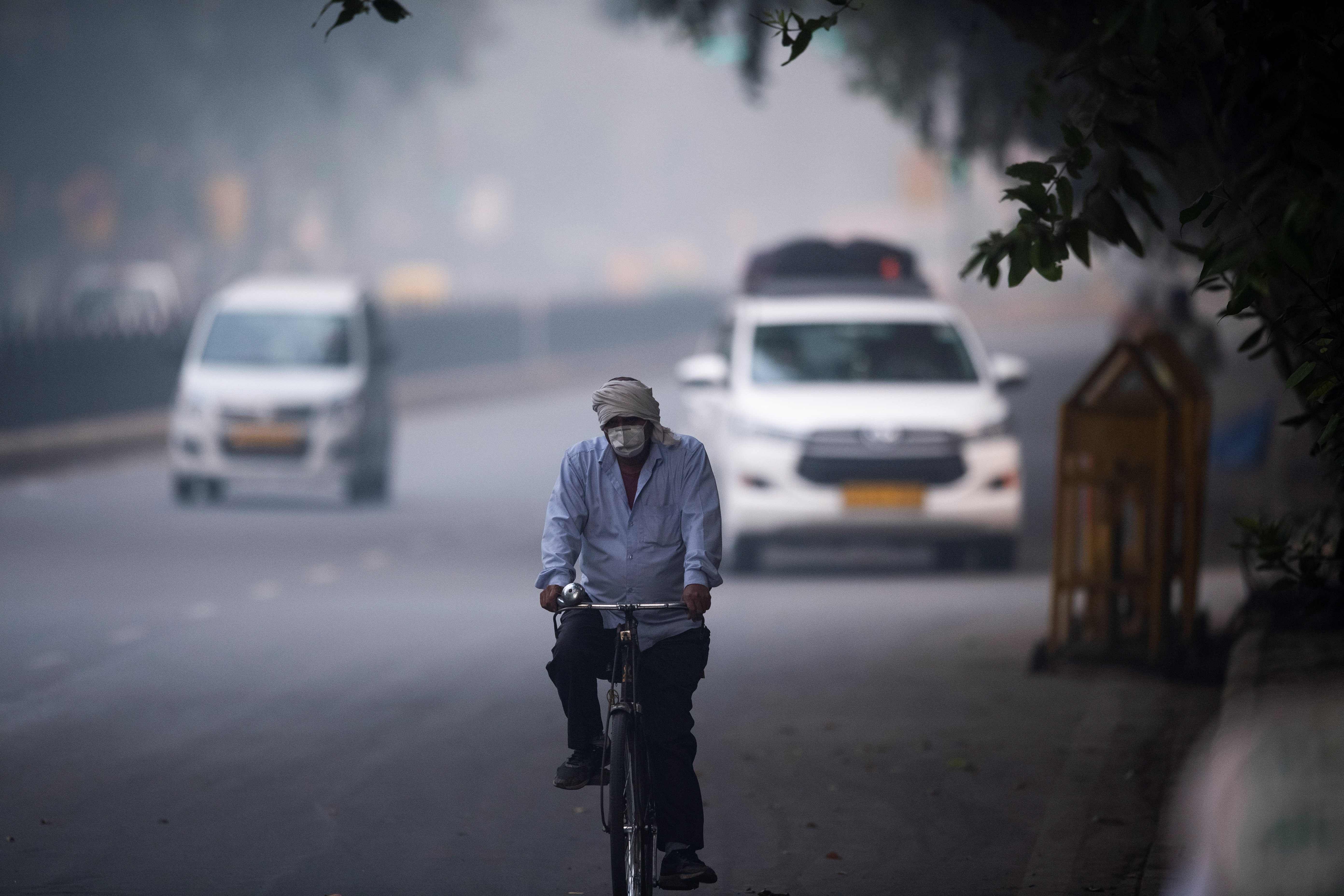 A man wearing protective face mask rides a bicycle along a street in smoggy conditions in New Delhi. (AFP Photo)