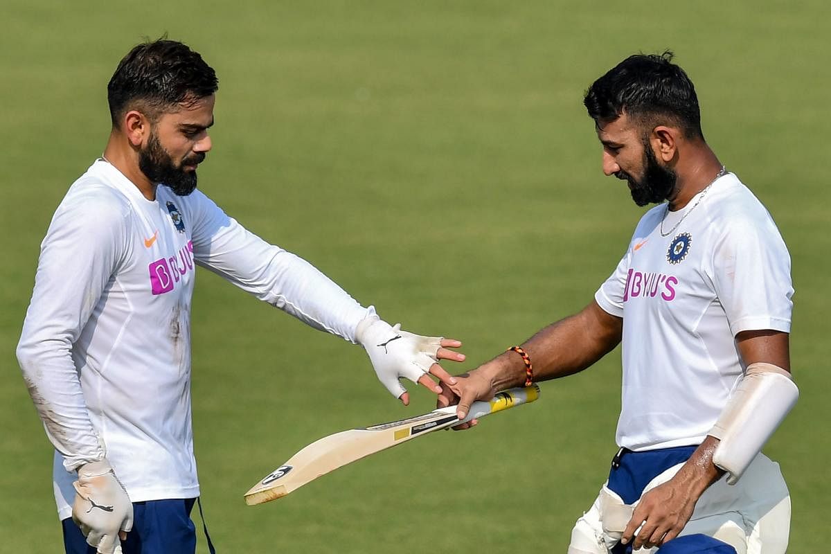 India's captain Virat Kohli (L) inspects teammate Cheteshwar Pujara's bat during a training session ahead of the first test match between India and Bangladesh at Holkar Cricket Stadium in Indore on November 12, 2019. (Photo by Indranil MUKHERJEE / AFP)