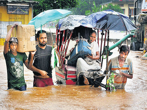 People wade through water logged streets of Anil Nagar after heavy showers in Guwahati on Monday. PTI