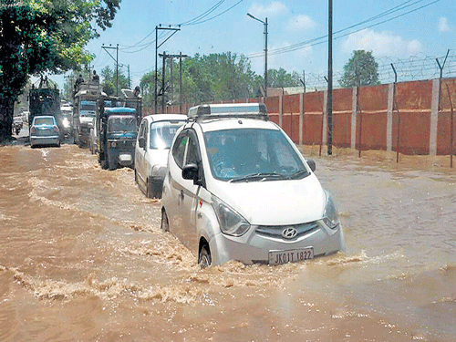Vehicles move through a flooded road following heavy rains in Srinagar on Friday. PTI