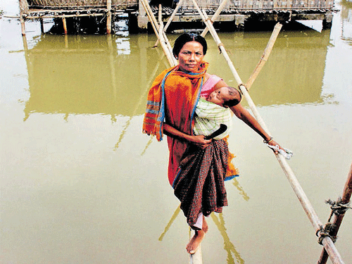 A woman, carrying her kid, uses a bamboo bridge to commute in a flood-hit village at Teok in Jorhat district of Assam on Saturday. PTI