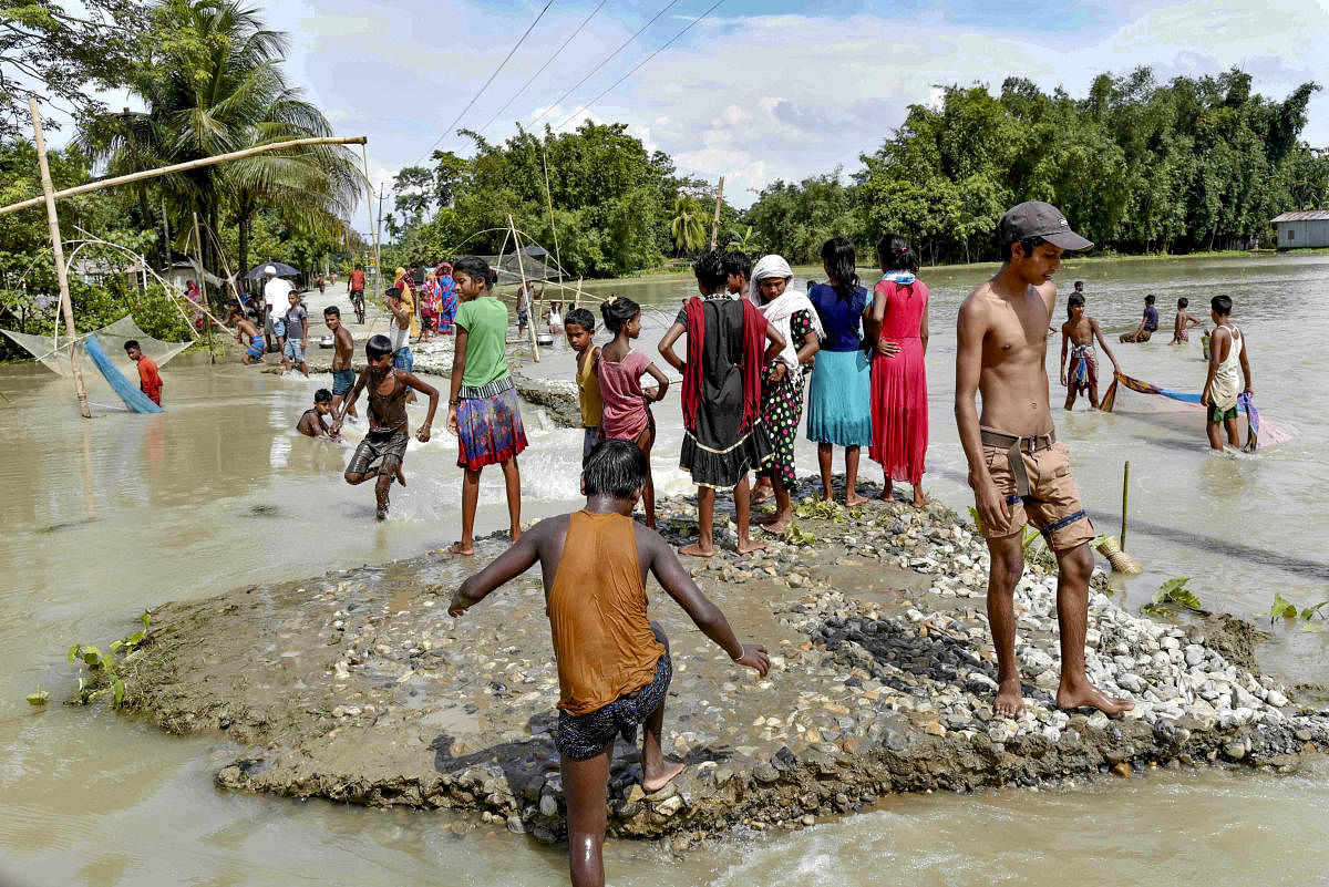 People walk through a flooded area after the Pahumara river overflowed, following heavy monsoon rain, in Barpeta district of Assam (PTI Photo)