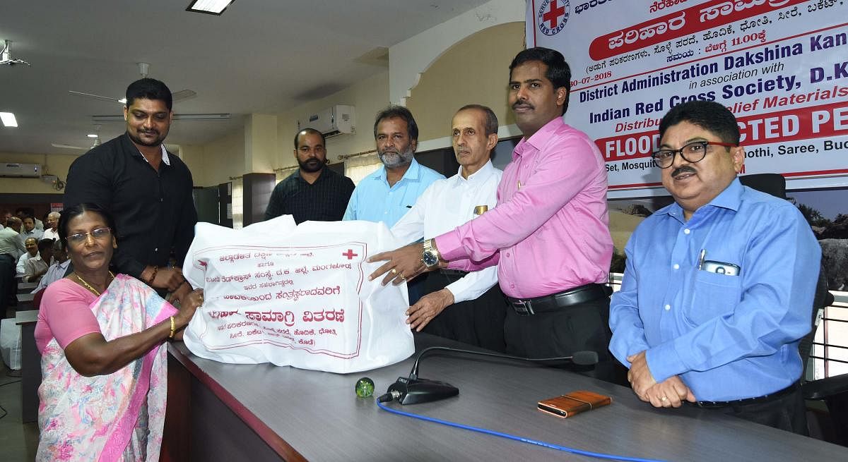 Additional Deputy Commissioner Kumar distributes a kit to one of the survivors of Mangaluru floods at the deputy commissioner’s office on Monday.