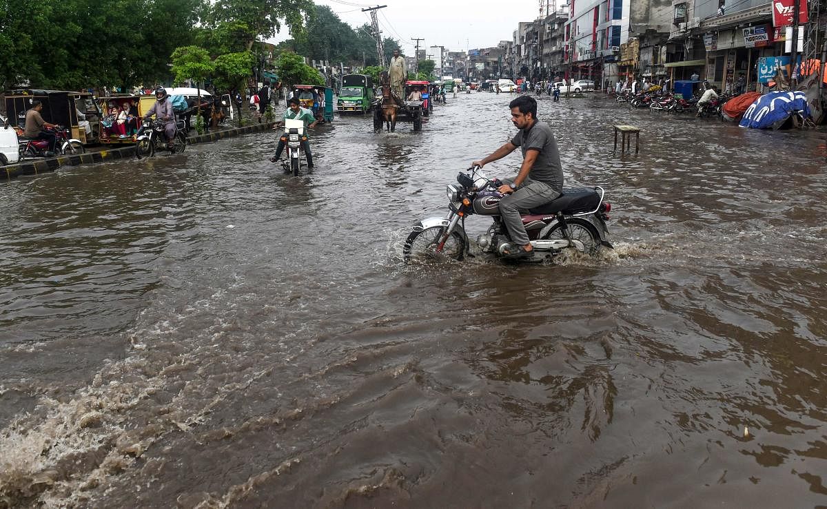 Commuters and pedestrians cross a flooded street after the monsoon rains in Lahore on July 20, 2019. (Photo by AFP)