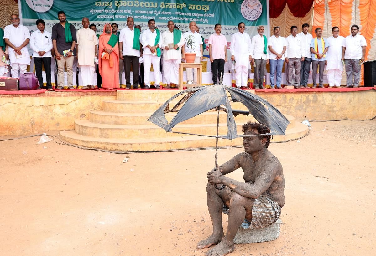 Raitha Sangha member protesting with a tattered umbrella against the state and Union governments demanding flood relief for farmers. DH Photo.