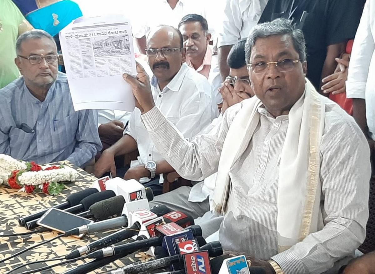 Opposition Leader Siddaramaiah displays a copy of a report on flood-hit victims, during a press conference, in Mandya, on Thursday. Ex-minister M S Athmananda is seen.