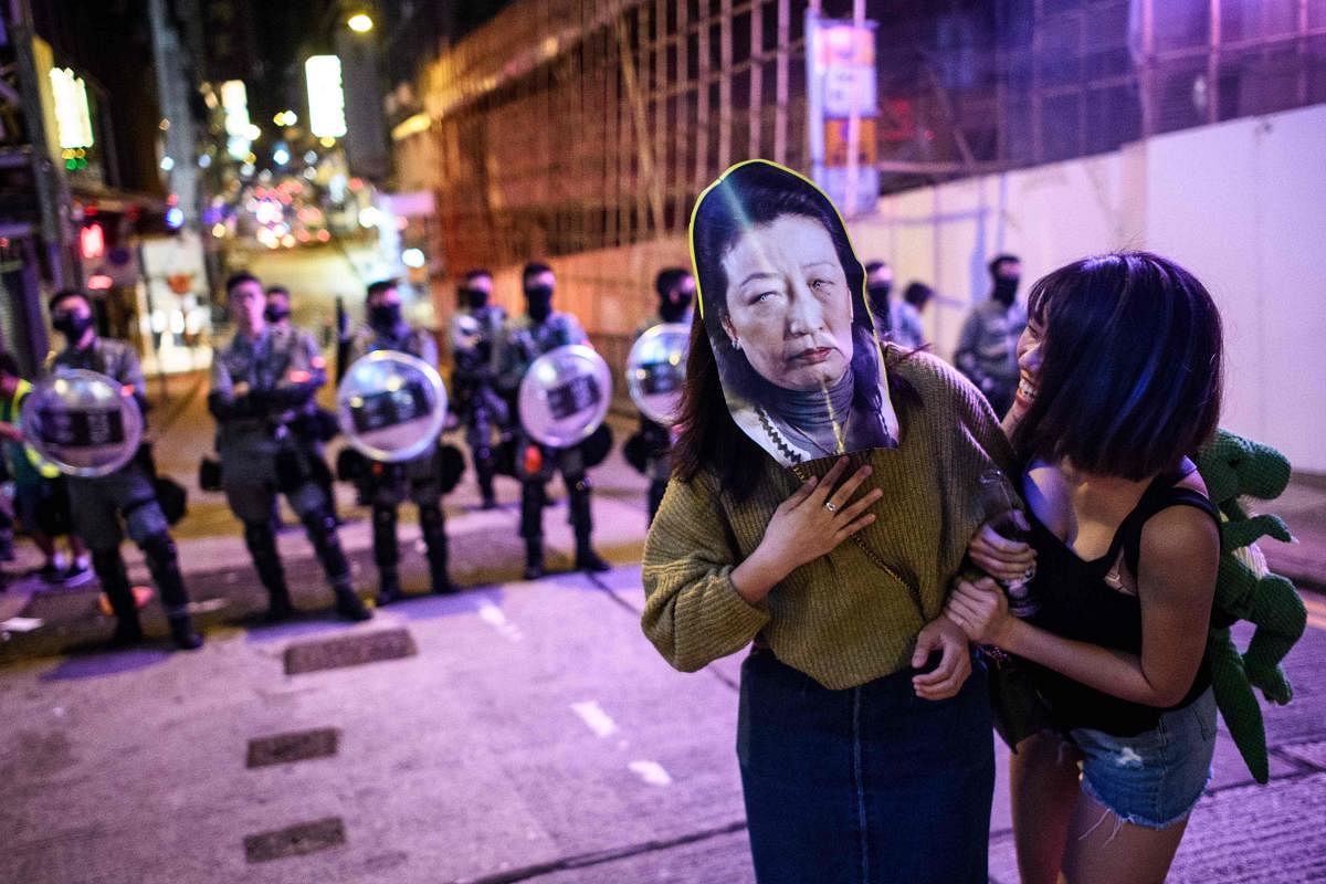 A woman wears a face mask depicting Secretary for Justice Teresa Cheng as she poses for photos in front of a line of riot police (AFP Photo)