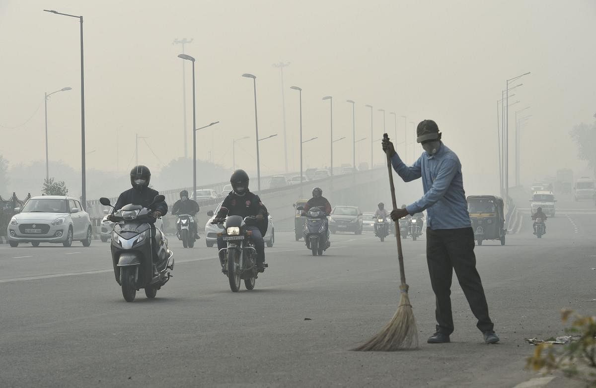 A civic worker, wearing an anti-pollution mask, sweeps the road amid heavy smog, in New Delhi. (PTI Photo)