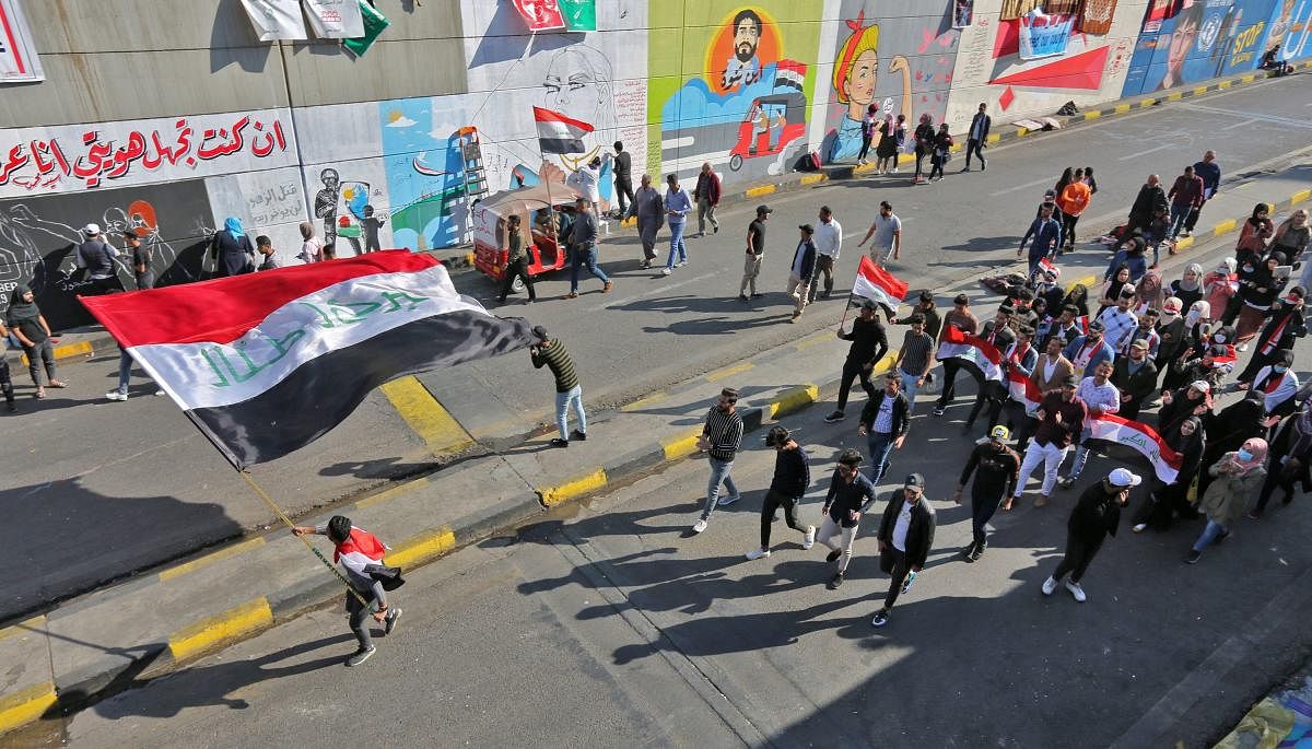 Iraqi youths waving national flags march through Tahrir Square in the Iraqi capital Baghdad as anti-government protests continued across the country. (Photo by AFP)