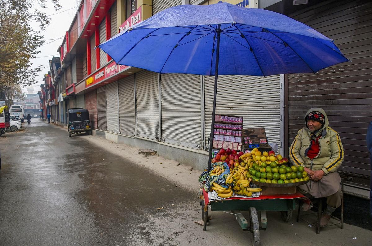A vendor sells fruits outside closed shops at market during shutdown in Srinagar. (PTI Photo)