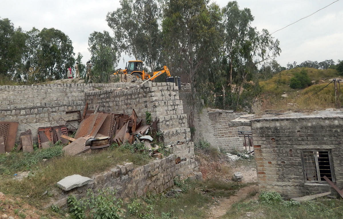 Forest department officials demolish the structures with excavators, at the illegal crushing units in Srirangapatna, Mandya district on Friday.